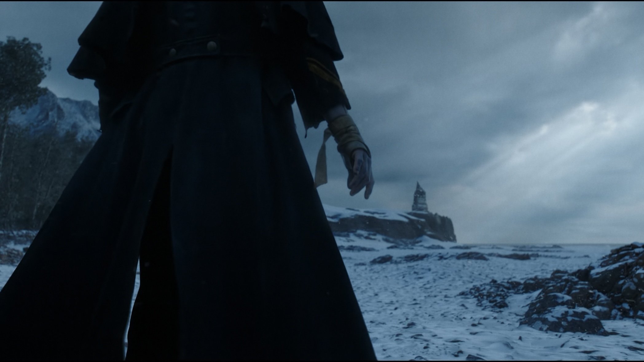 Caption: a man in a long black coat standing in the snow