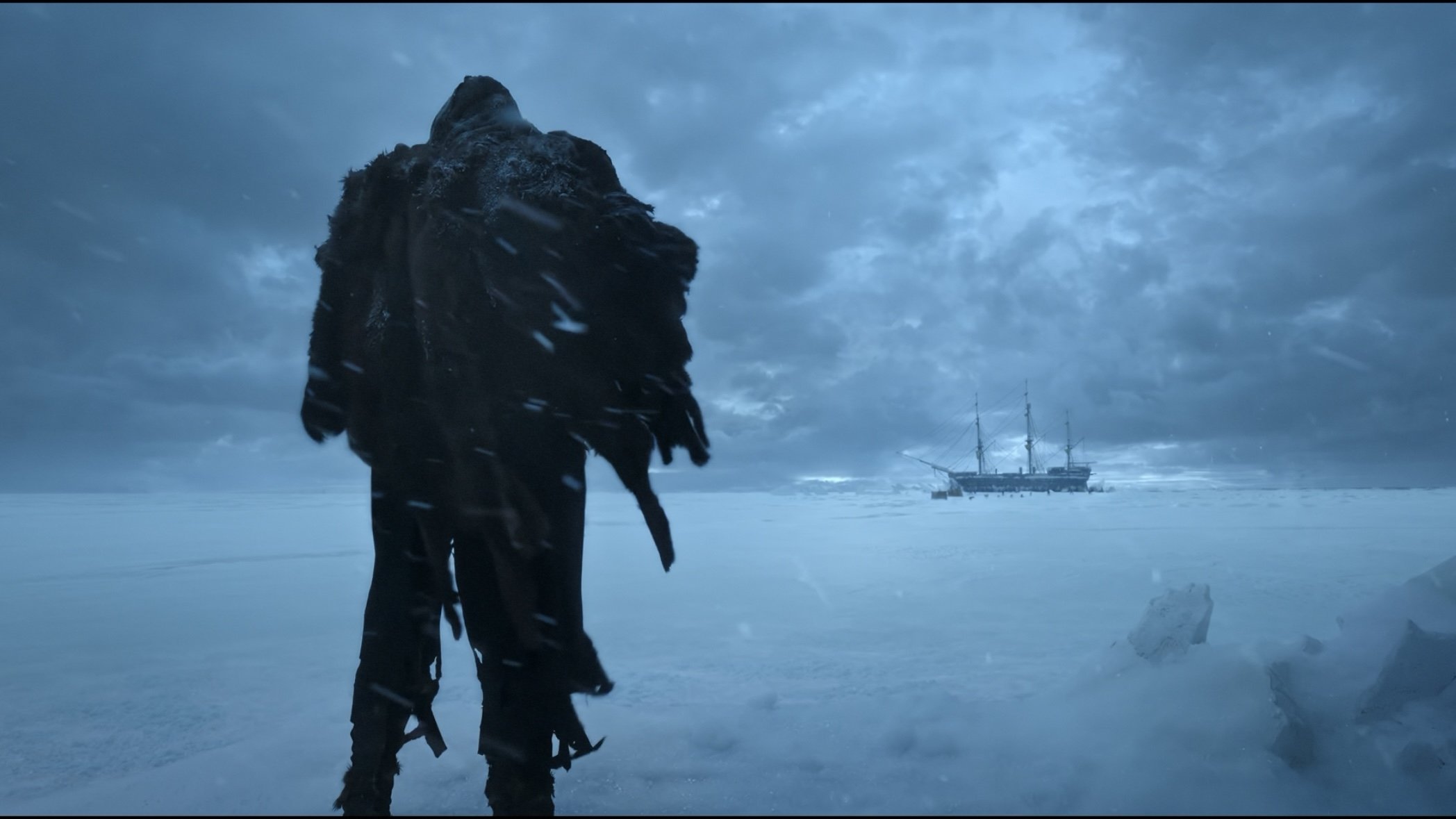 Caption: a person standing in the snow with a ship in the background