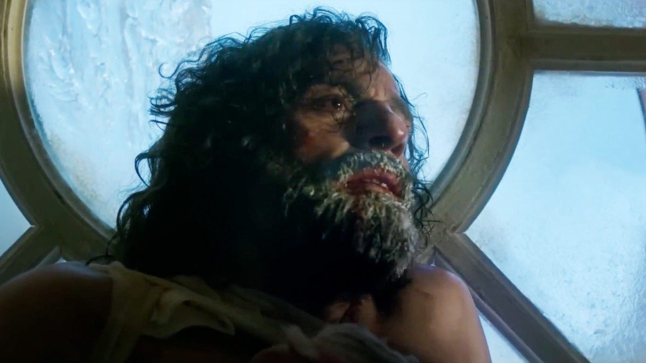 Caption: a man with long hair and a beard standing in front of a round window