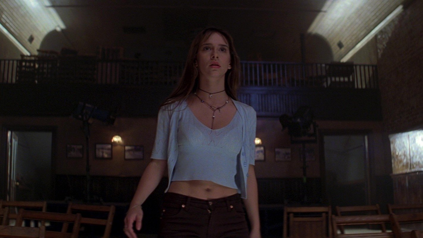 Caption: a woman standing in a room with wooden chairs