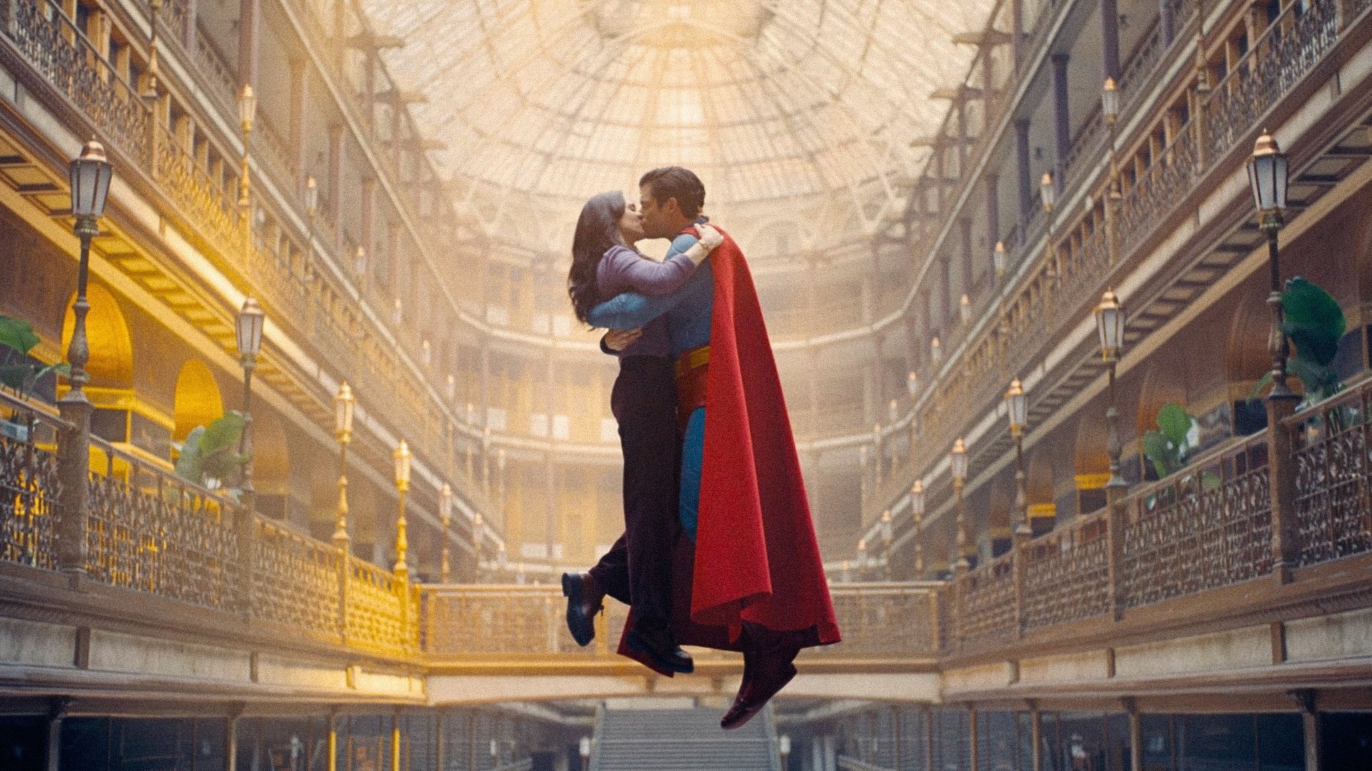 Caption: a man and a woman dressed as superman kissing in a building