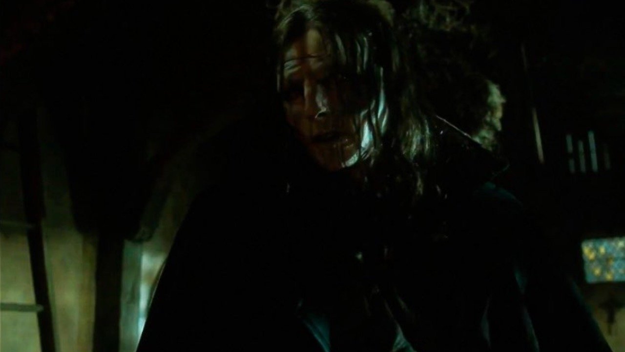 Caption: a man with long hair standing in a dark room