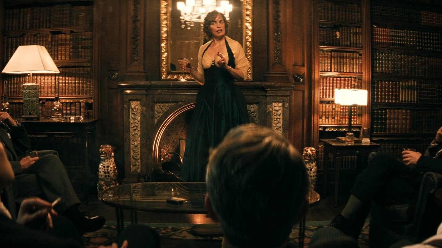 Caption: a woman in a black dress standing in front of a room full of people