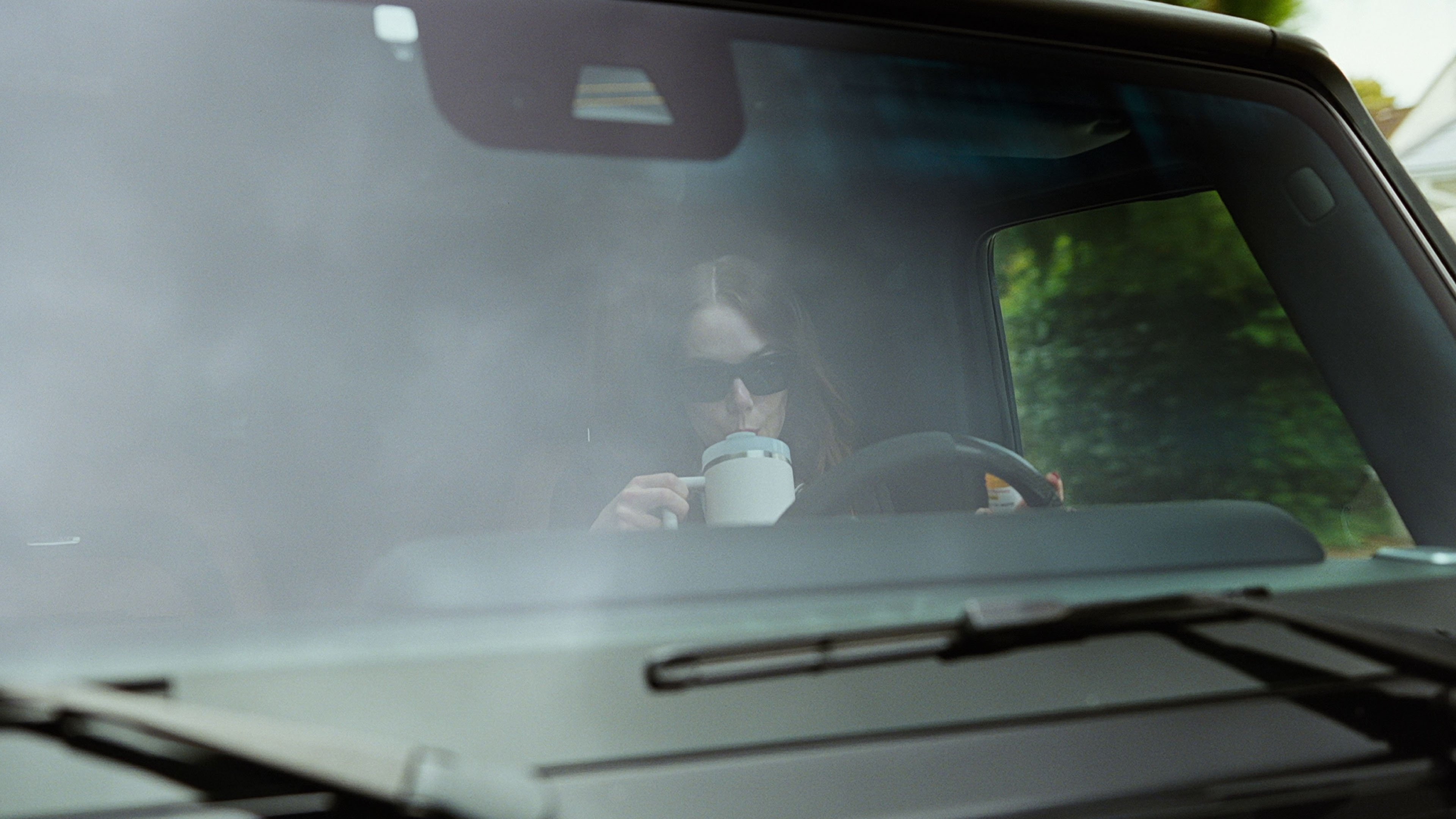 Caption: a woman sitting in a car drinking from a cup