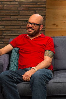 David Cross Wears a Red Polo Shirt & Brown Shoes with Red Laces
