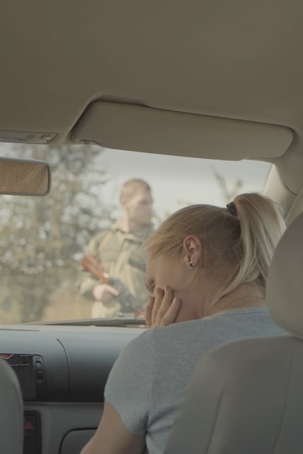 A young family is driving down a road that is blocked by armed soldiers. The soldiers stop the car for no reason and take the man away for questioning. The man's wife and daughter stay in the car, waiting.